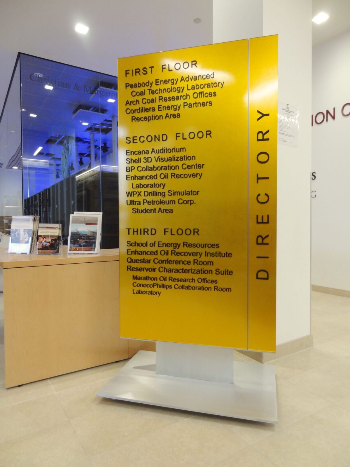 A yellow directory sign in a building lists the floor details: First Floor - various energy and environmental labs, and offices; Second Floor - aviation, space labs, and resources; Third Floor - systems, transportation resources, and cybersecurity.