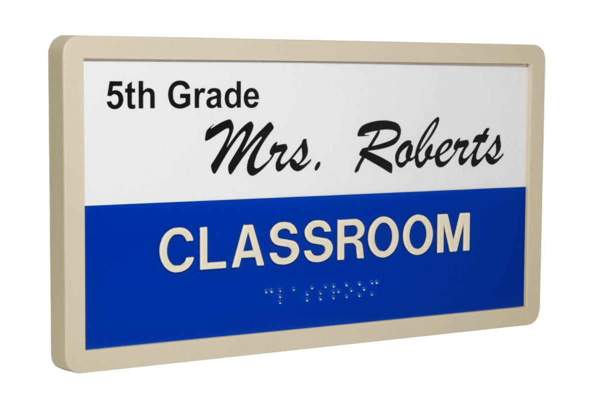 A sign with beige frame reads "5th Grade Mrs. Roberts CLASSROOM" in black and white text on a blue and white background. Braille text is below the word "CLASSROOM".