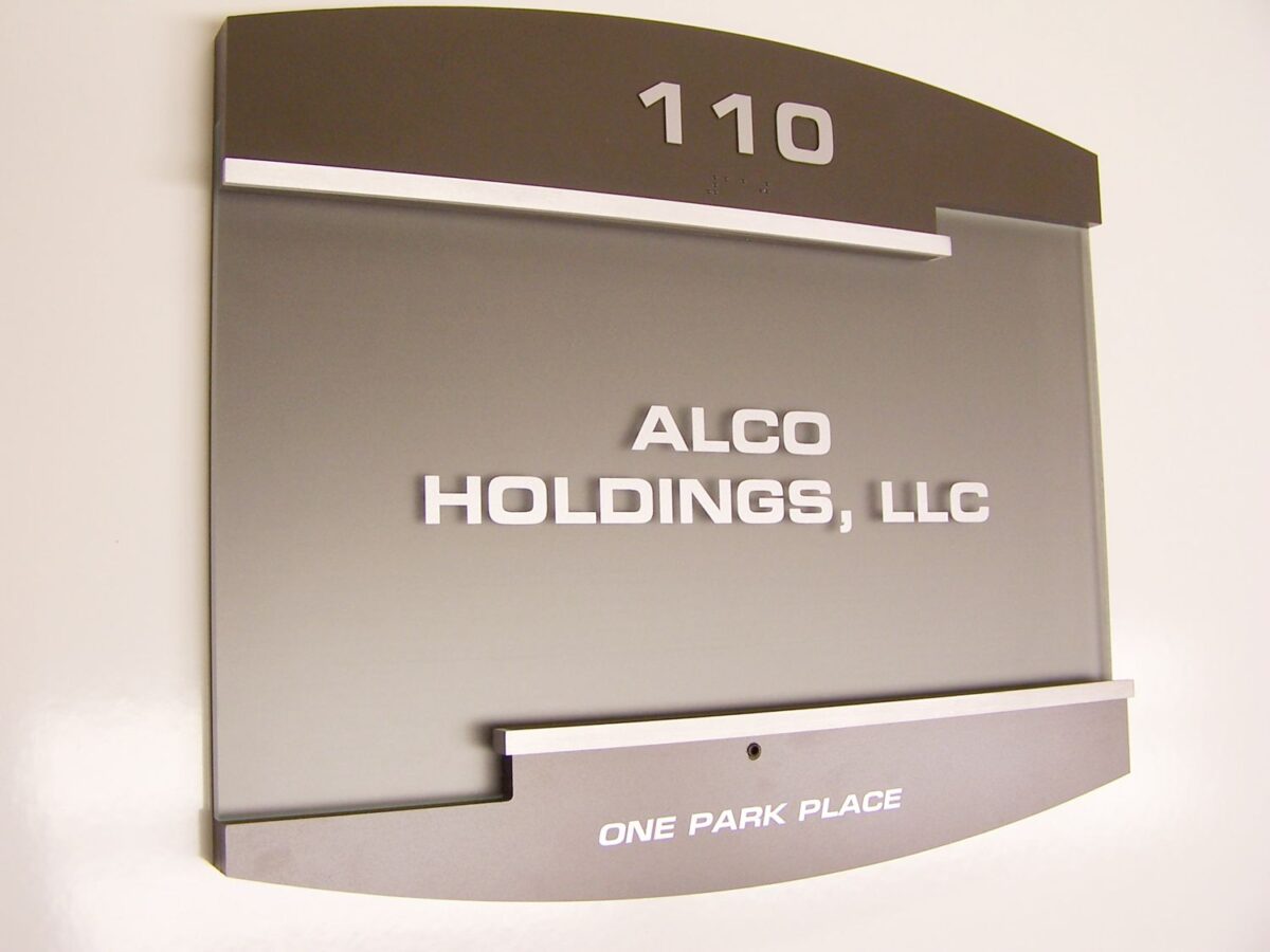 A door sign with the number "110" at the top. Below, it reads "ALCO HOLDINGS, LLC" in white capital letters. At the bottom of the sign, it says "ONE PARK PLACE." The sign has a modern style with a metallic finish and white text.
