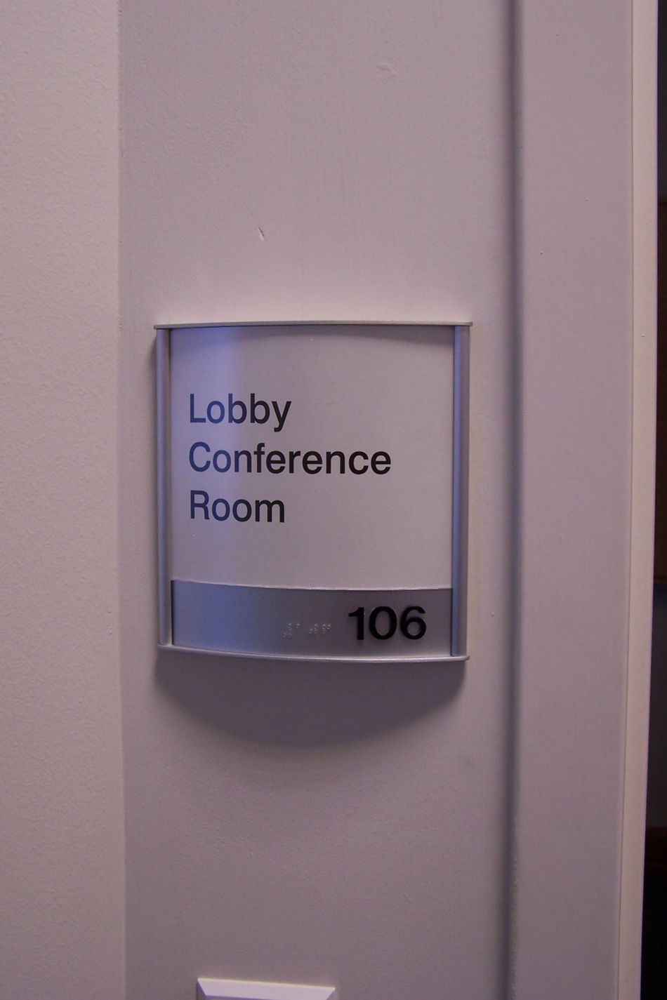 A small rectangular wall sign reads "Lobby Conference Room" with the number "106" displayed beneath it. The sign is mounted on a light-colored wall, indicating the room's location and purpose within a building.