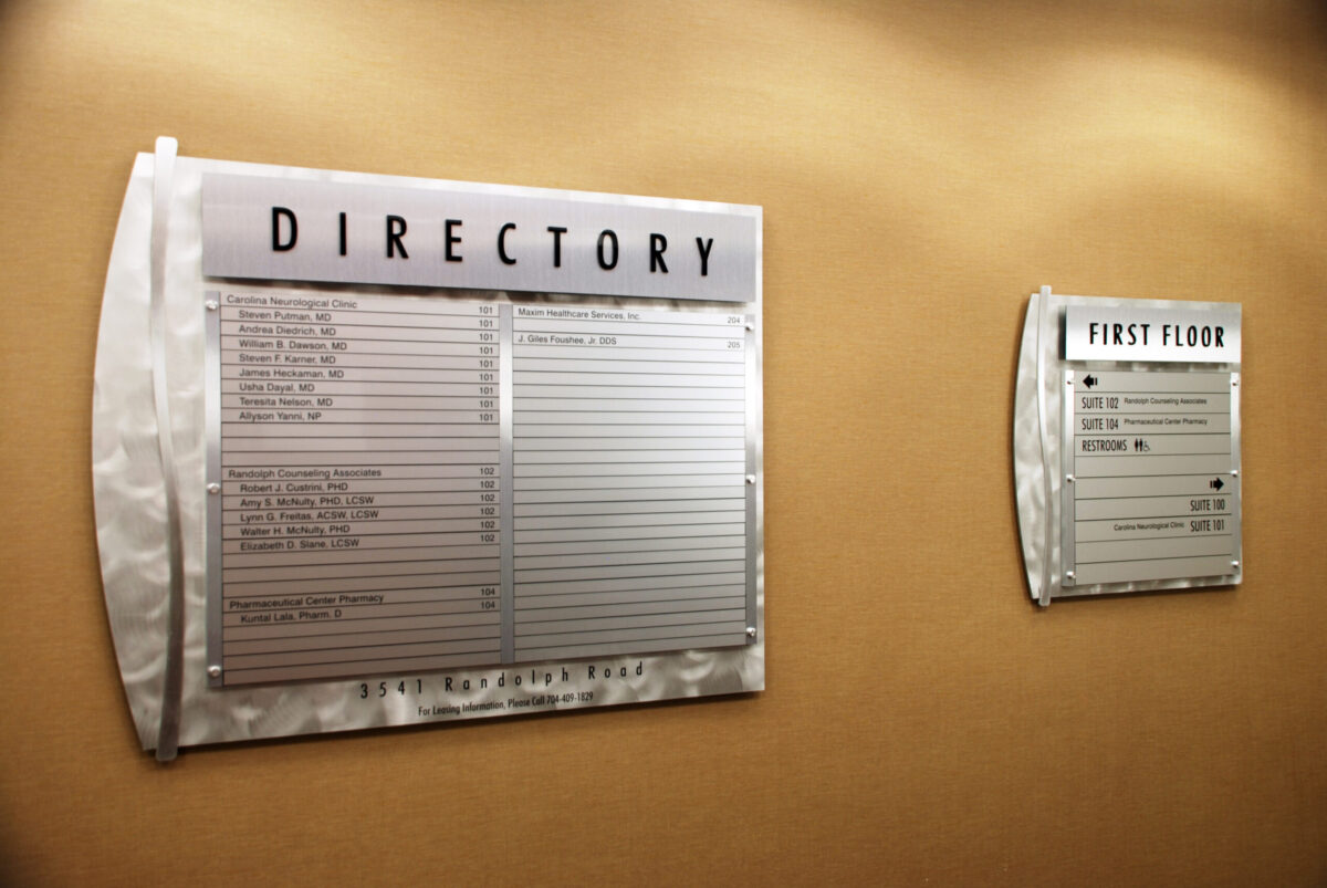 A directory board on the left lists the locations of various departments or offices, while a first floor directory on the right provides a smaller, focused list of locations specifically for the first floor. Both directories are mounted on a beige wall.