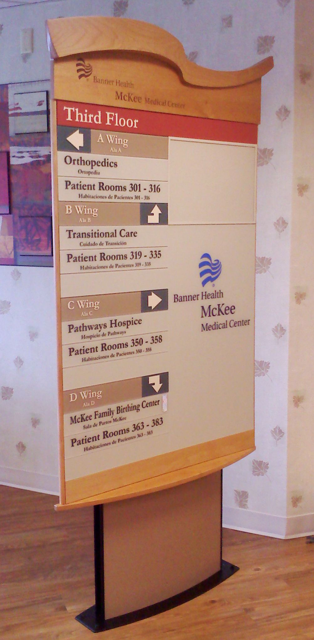A stand-up directory sign in an indoor setting indicates locations within McKee Medical Center. The sign lists various departments on the third floor, including Orthopedics, Transitional Care, and Pulmonary. The background features soft-colored wallpaper.