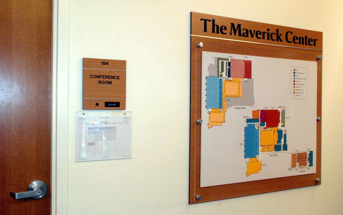 A wall-mounted map of The Maverick Center with various colored sections. To the left, there is a door with a sign that reads "Conference Room" and a small clipped sheet beneath it. A door handle is visible at the bottom left.