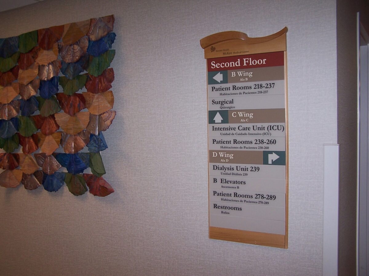 A directory sign on a wall shows the layout of the second floor in a hospital. It indicates the locations of various wings, patient rooms (200-237), surgical and intensive care units, and dialysis units. A colorful leaf-shaped wall decoration is seen beside the sign.