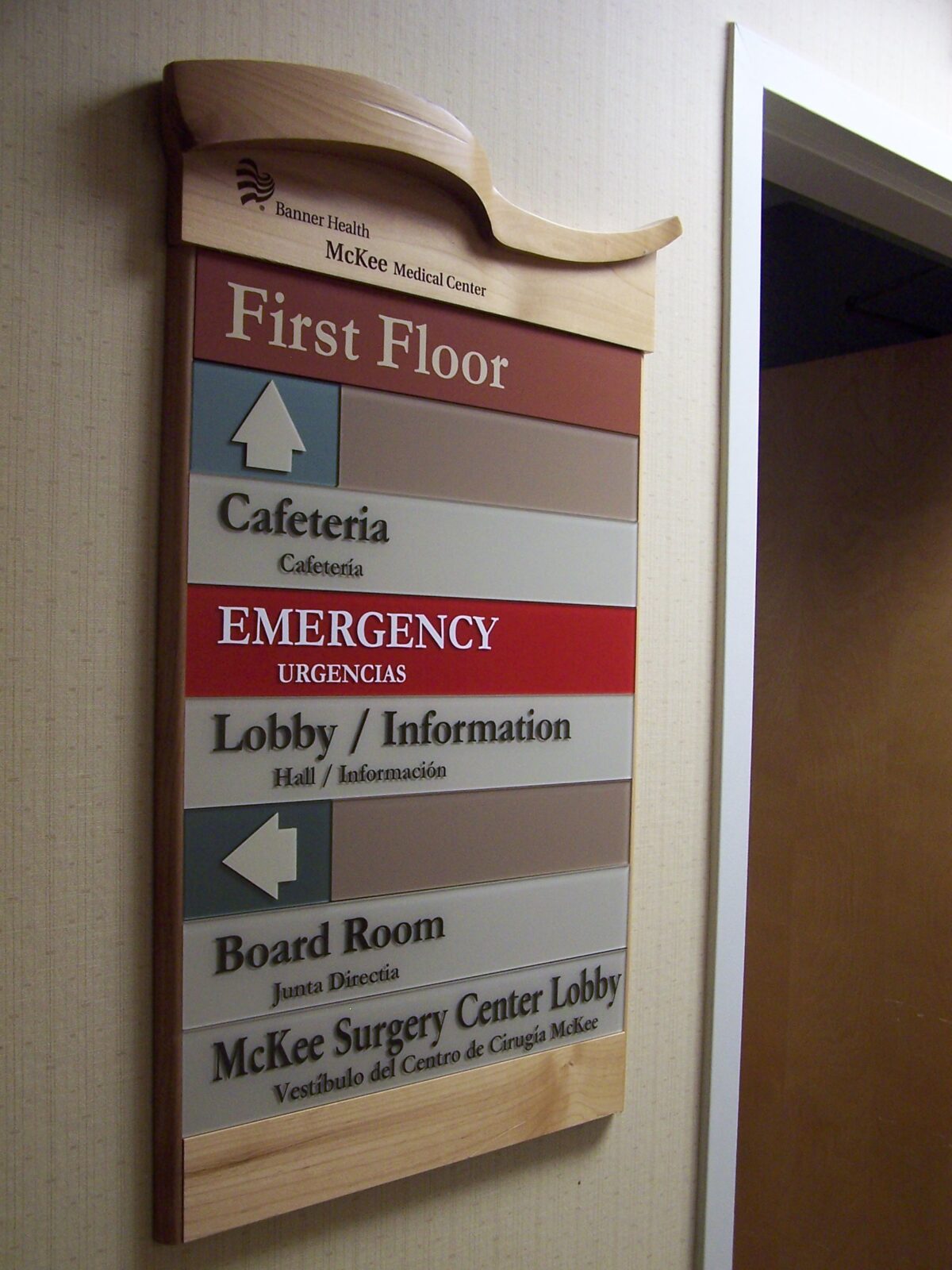 A wall-mounted directory sign inside a building, indicating locations on the first floor. It lists the cafeteria, emergency, lobby/information, board room, and McKee Surgery Center lobby with arrows pointing the directions to each area.