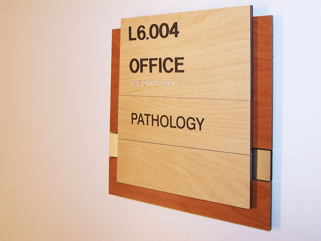 A wall-mounted office sign with a wooden frame and beige panels. The top panel reads "L6.004." The middle panel reads "OFFICE," and the bottom panel reads "PATHOLOGY.