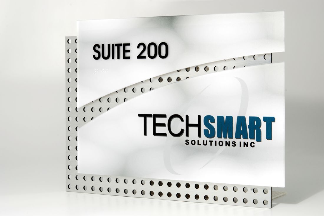 A sign for TechSmart Solutions Inc. The sign features the text "SUITE 200" at the top and "TECHSMART SOLUTIONS INC" at the center. The background has a sleek design with perforated metal elements and smooth white panels.