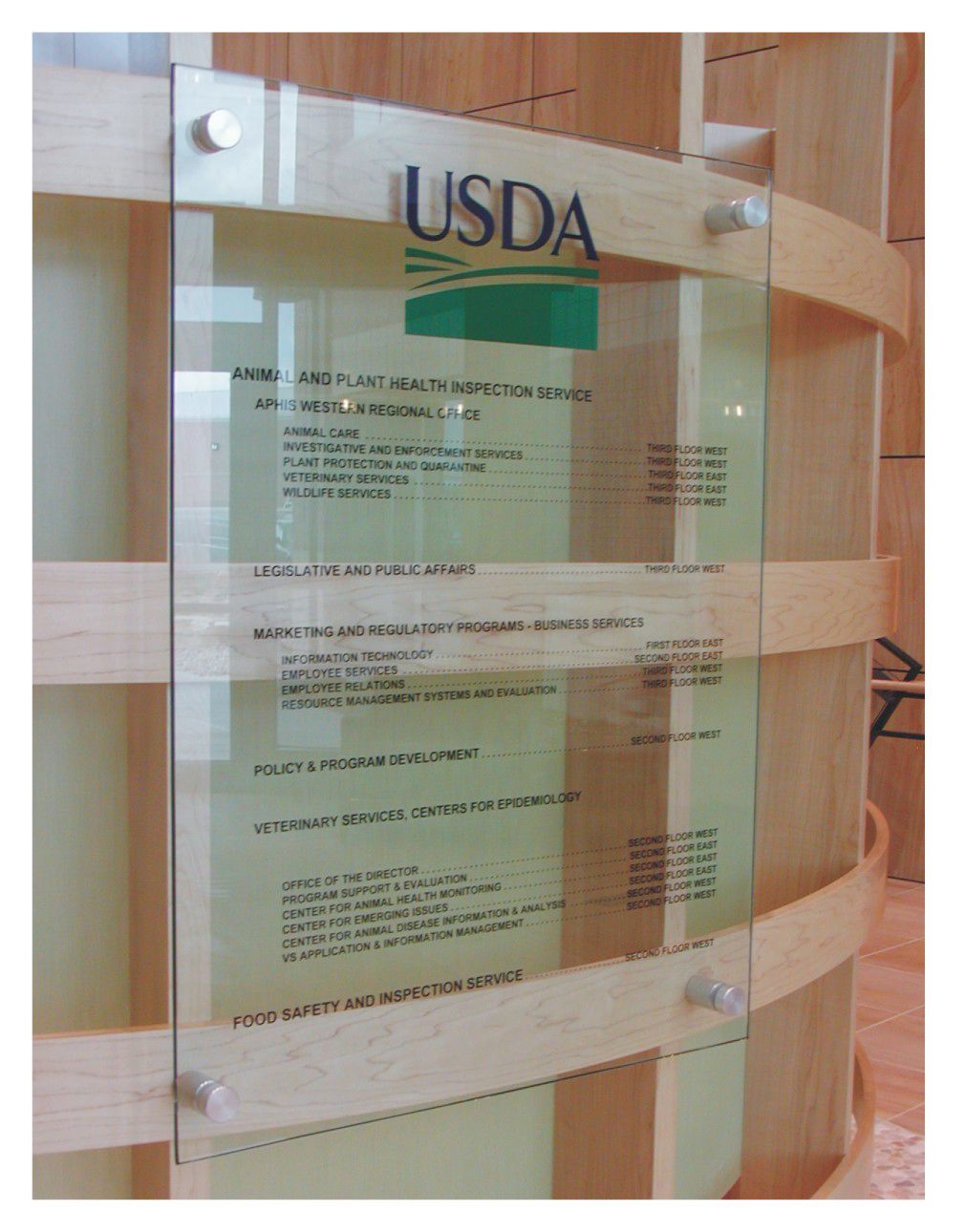A frosted glass directory inside a wooden frame displays information beneath the USDA logo. The text outlines various services, including Animal and Plant Health Inspection, Grain Inspection, and Food Safety and Inspection. The background features wood paneling.