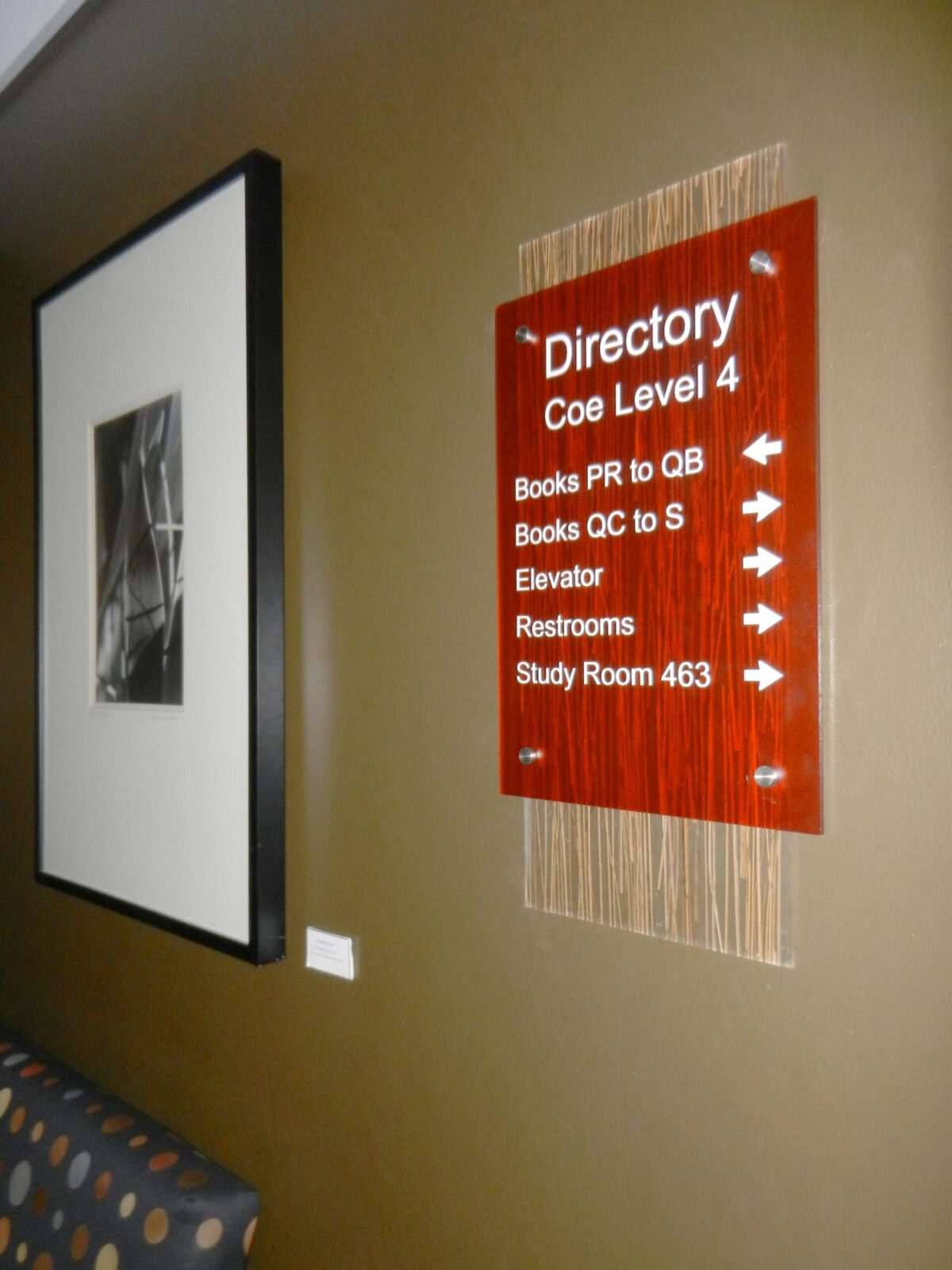 A wall-mounted directory sign on Coe Level 4 with arrows pointing to "Books PR to QB," "Books QC to S," "Elevator," "Restrooms," and "Study Room 463." Next to the sign is a framed black-and-white photograph.