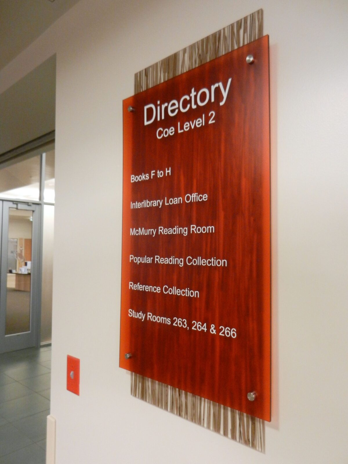 A red wall-mounted directory sign on Coe Level 2 lists several locations: Books F to H, Interlibrary Loan Office, McMurtry Reading Room, Popular Reading Collection, Reference Collection, and Study Rooms 263, 264, & 266. An exit sign is visible below it.