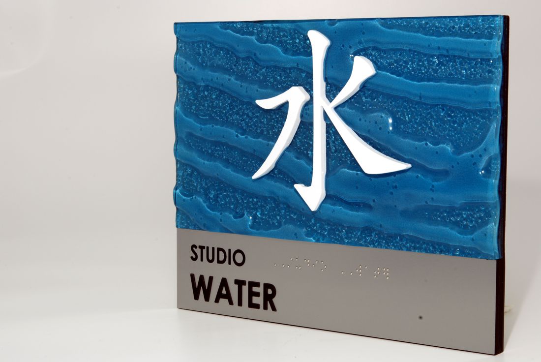 A sign with a blue background featuring textured, wave-like patterns and a prominent white Chinese character for "water." Below the blue section, there's a gray section with the words "STUDIO WATER" in black lettering.