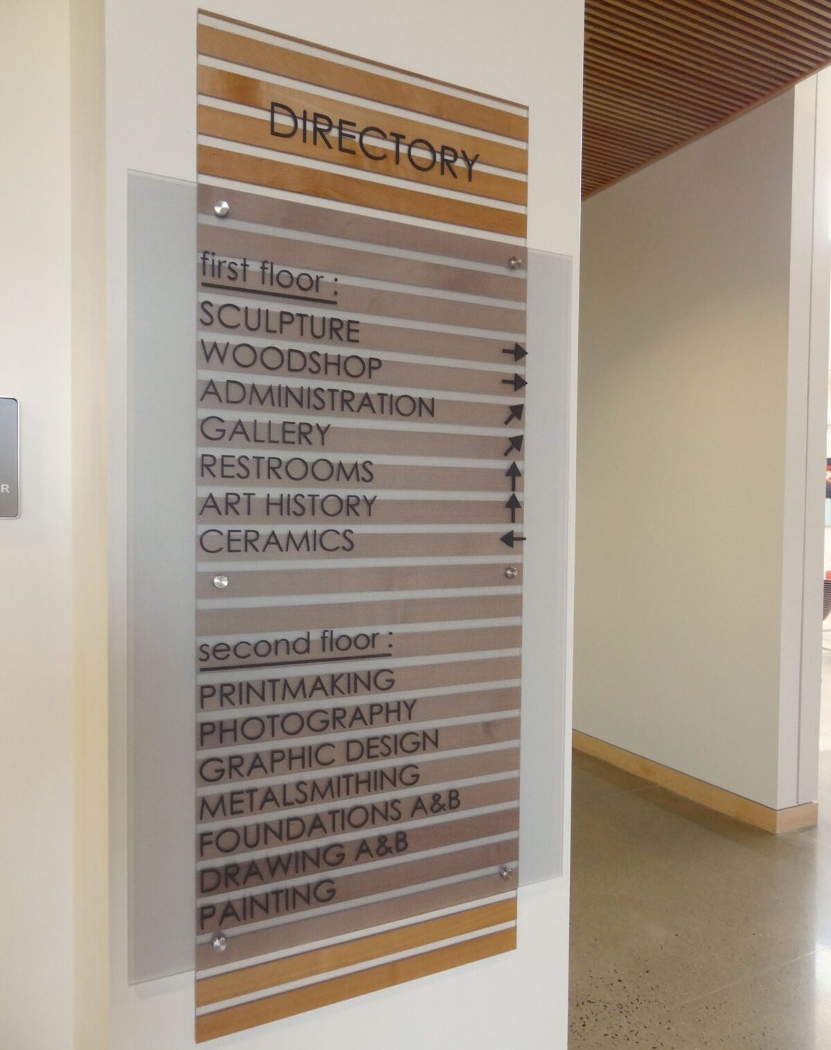 A wall-mounted directory sign lists sections for two floors. The first floor includes Sculpture, Woodshop, Administration, Gallery, Restrooms, Art History, and Ceramics. The second floor lists Printmaking, Photography, Graphic Design, Metalsmithing, Foundations Asl, and Drawing/Painting.