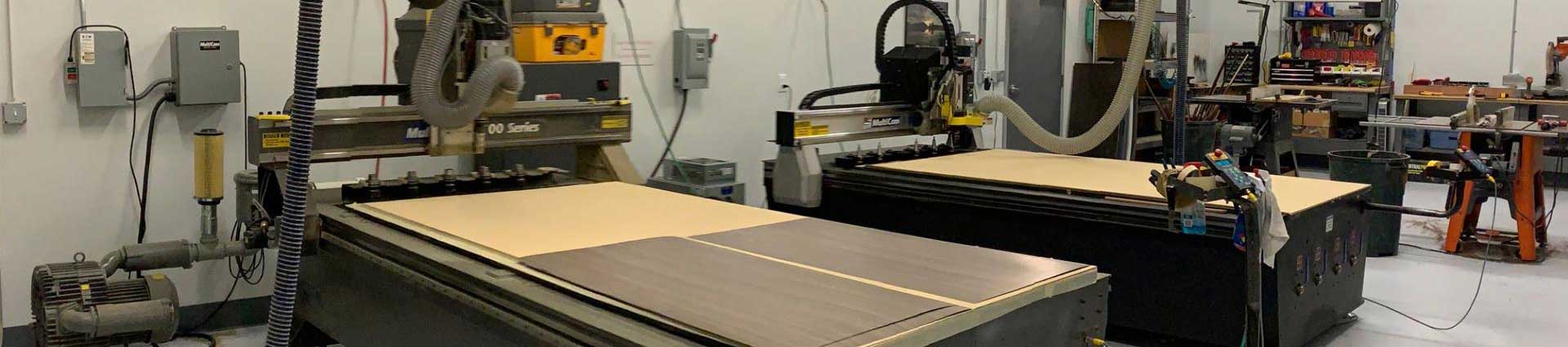A wide-angle view of a well-equipped workshop featuring multiple CNC machines and other equipment, showcasing a large wood cutting CNC in the foreground, highlighting the industrial capabilities of the facility