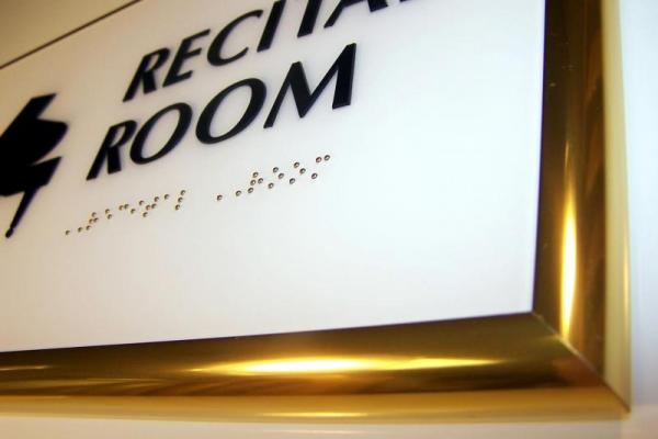 Close-up of a recital room sign in a frame with braille text beneath the print