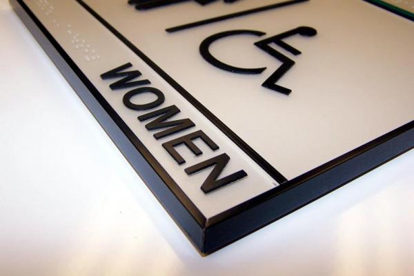 Sleek, modern restroom sign for women with accessible iconography and braille text.