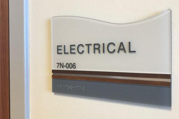 Curved wall sign reading 'ELECTRICAL 7N-006' with a modern design, incorporating wood and metallic elements.