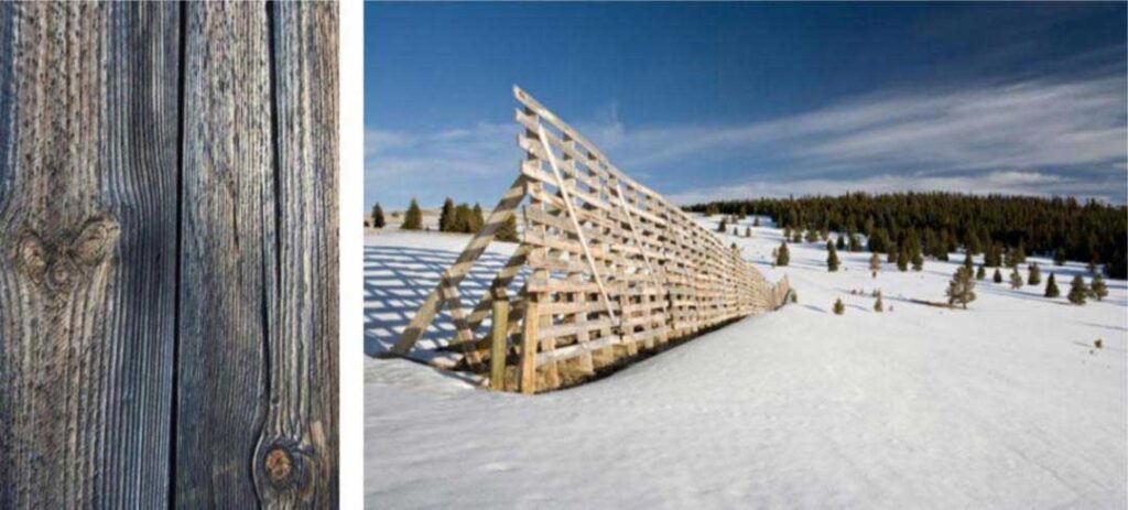 Landscape showing a large wooden snow fence spanning across a snowy field with a forest in the background