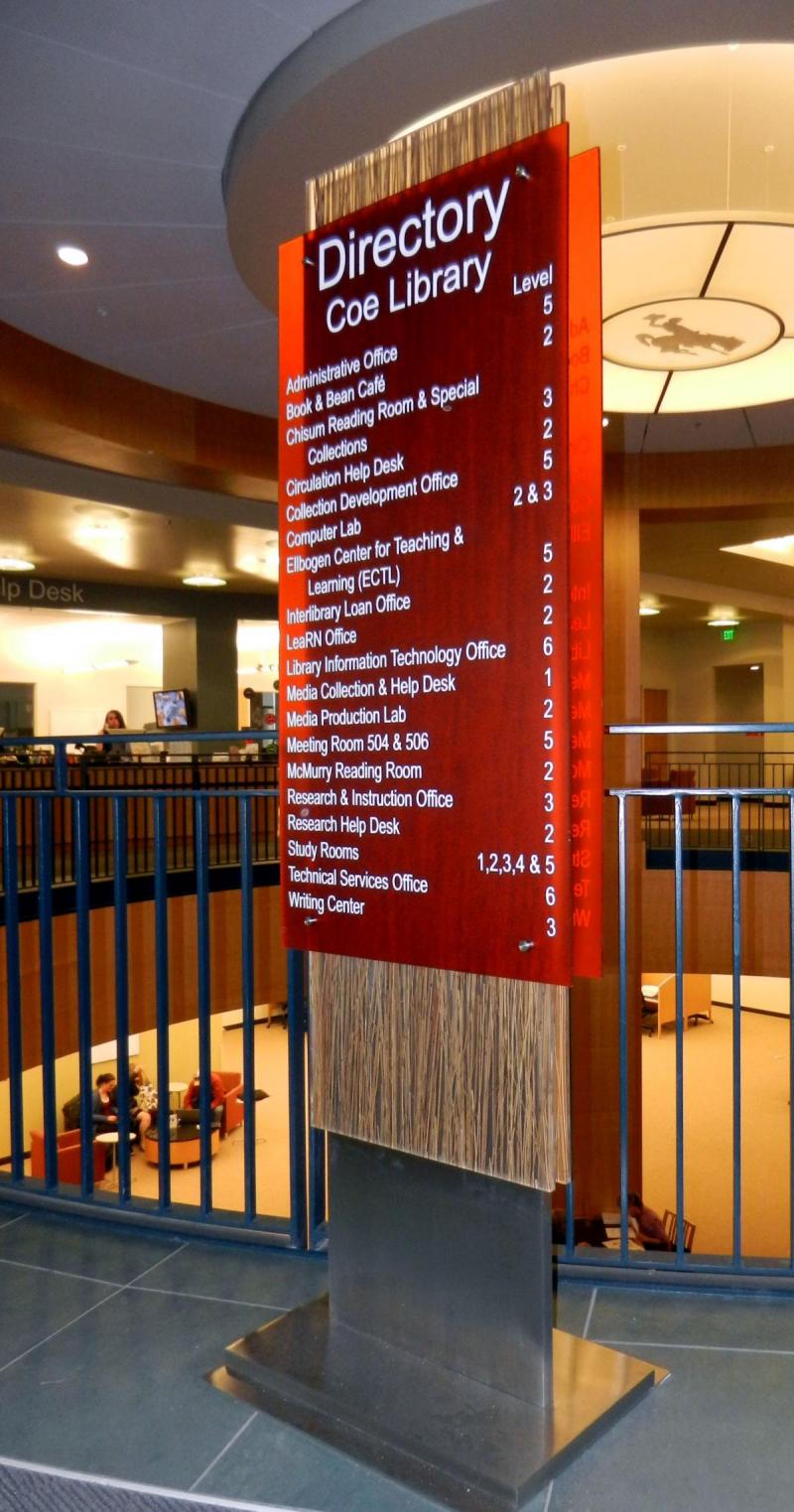 Tall directory sign inside Coe Library listing various departments like Administrative Office, Book & Bean Café, and Study Rooms with their corresponding levels, situated in a spacious atrium.