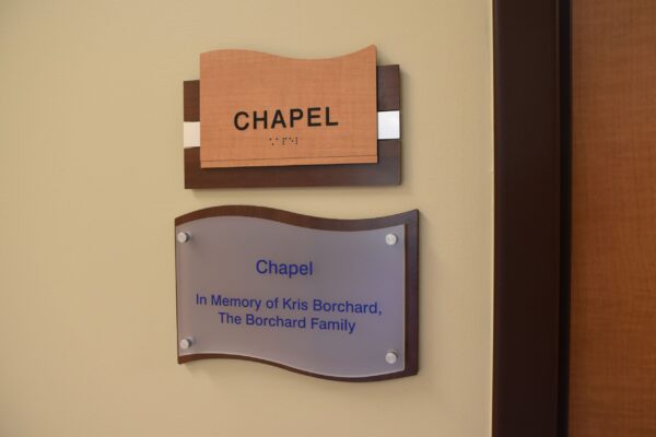 A sign indicating the location of a chapel. The top sign has "CHAPEL" written on it in bold letters. Below it, a plaque reads "Chapel in Memory of Kris Borchard, The Borchard Family".