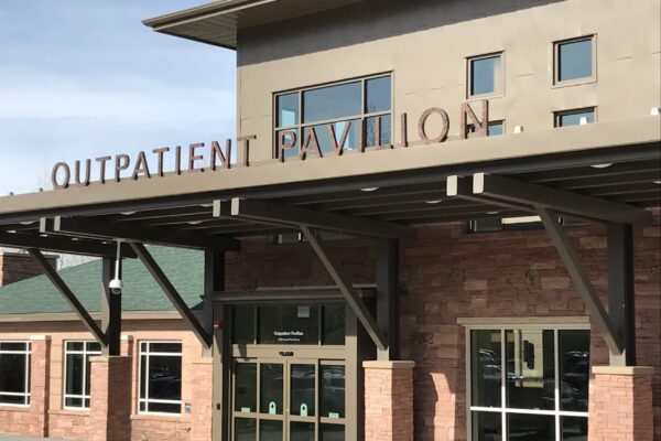 A tan and brick building with a sign reading "OUTPATIENT PAVILION" above the entrance. The entrance has glass doors and large windows, and a covered walkway extends from the building.