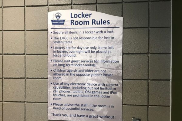 A poster titled "Locker Room Rules" is displayed on a tiled wall. The rules include securing items with a lock, the facility not being responsible for lost or stolen items, and guidelines for daily locker use, guest services, and electronic devices.