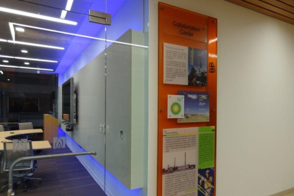 A modern office conference room with glass walls, featuring a blue-lit interior. Outside the room, on the right wall, there are informational posters about climate change with images and text. The area is well-lit and has a clean, professional appearance.