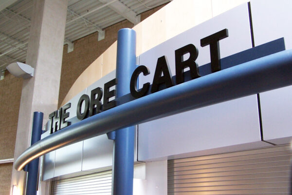 A modern storefront with a sign reading "THE ORE CART." The structure features sleek blue and silver designs, with a partially visible roller shutter door.