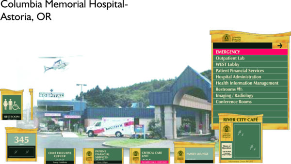 Image of Columbia Memorial Hospital in Astoria, OR. The entrance features a sign with multiple departments listed, including Emergency, Outpatient Lab, Patient Financial Services, and Radiology. An ambulance is parked, and a helicopter is in the sky above.
