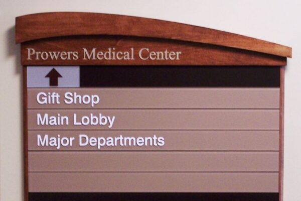 A directory sign at Prowers Medical Center shows directions to the Gift Shop, Main Lobby, and Major Departments, with an arrow pointing upwards. The sign has a wooden header and beige background.