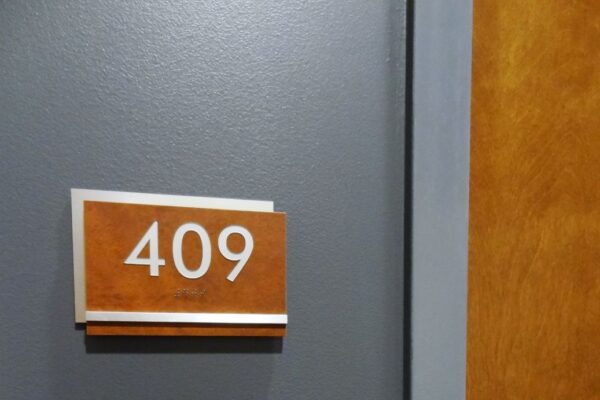 A grey door with a room number sign that reads "409" in white text on a rust-colored background is partially open, revealing part of a wooden door frame and a metal door handle.