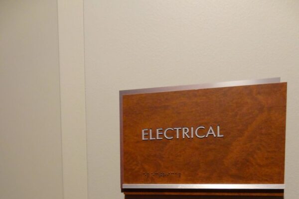 A beige door slightly ajar with a silver handle, displaying a wooden sign that reads "ELECTRICAL" in white letters.