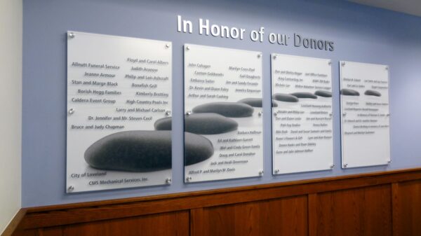 Four plaques on a wall honor donors. Each plaque lists multiple names under the heading "In Honor of Our Donors." The plaques are mounted on a light blue wall above a wooden panel.