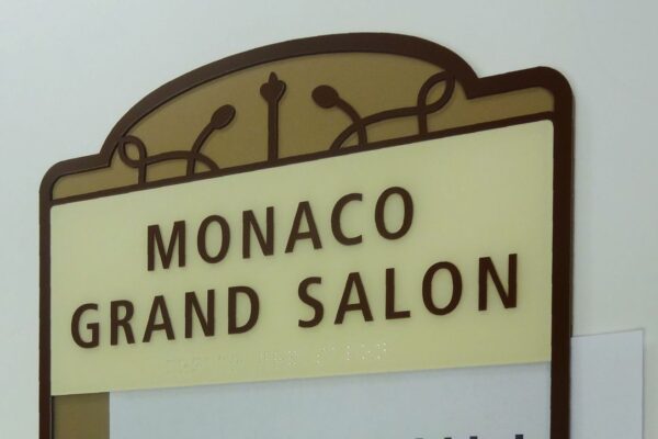A sign for the "Monaco Grand Salon" with an insert underneath that reads, "International Living Seminar, 8:30am - 4:00pm, May 8th." The sign has a decorative border and the text is in a mixture of brown and black fonts on a beige background.