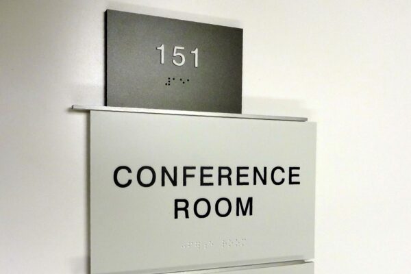 A white and grey conference room sign with the number 151 and Braille text at the top. The middle section reads "CONFERENCE ROOM," and a small sign at the bottom indicates "AVAILABLE" with a green dot next to it.