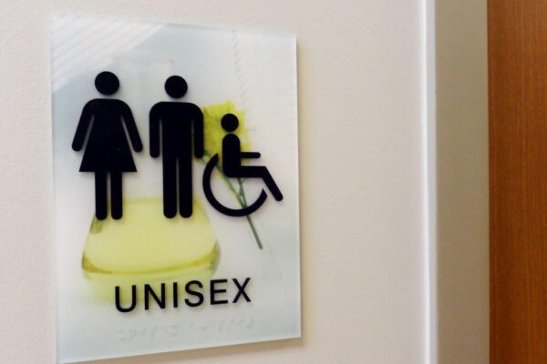 Sign on a wall labeled "UNISEX" with icons depicting a female figure, a male figure, and a person in a wheelchair, indicating an inclusive restroom.