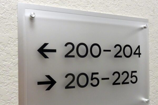 A frosted glass sign mounted on a wall indicates directions with black text: an arrow pointing left for rooms 200-204 and an arrow pointing right for rooms 205-225.