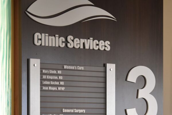 A wall directory sign for Clinic Services on the third floor. It lists Women's Care, General Surgery, and Anti-Aging Medical Spa with various names of doctors alongside each category. The sign is mounted on a dark wooden background.
