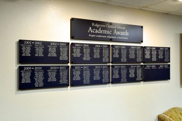 Plaques mounted on a wall display Ridgeview Classical Schools Academic Awards. Each plaque is titled with a school year and lists award recipients' names. The top plaque reads, "Ridgeview Classical Schools Academic Awards.