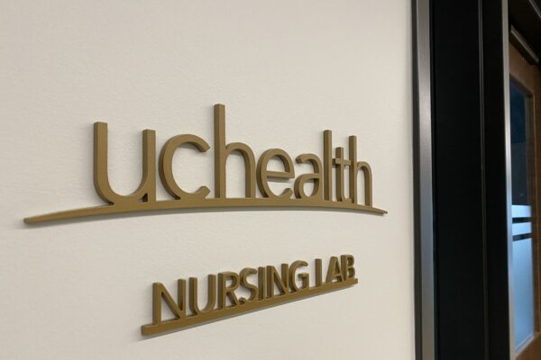 Wall sign reading "UCHealth Nursing Lab" in gold letters. The sign is affixed to a white wall near a dark-colored door frame.