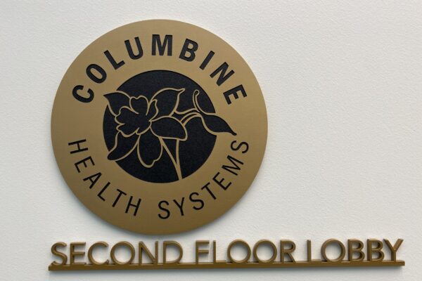A circular plaque displays "Columbine Health Systems" with a flower logo in the center, mounted on a wall. Below the plaque, "Second Floor Lobby" is written in raised letters.