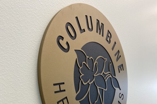 A circular plaque displays "Columbine Health Systems" with a flower logo in the center, mounted on a wall. Below the plaque, "Second Floor Lobby" is written in raised letters.