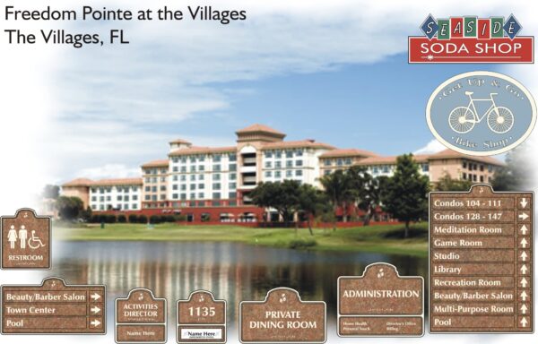 An image of the Freedom Pointe at the Villages in The Villages, FL, featuring a large building by a lake. Various signs indicate locations such as condos, a soda shop, bike shop, beauty salon, dining room, library, and more within the premises.