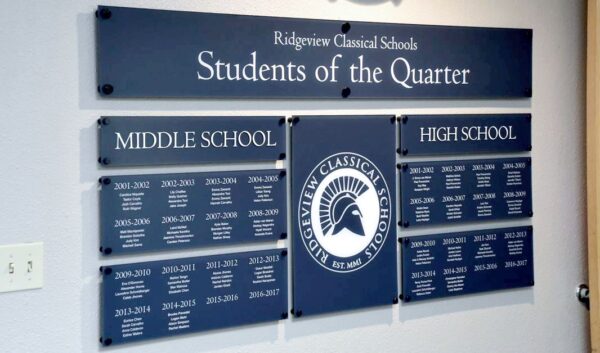 A wall display titled "Students of the Quarter" at Ridgeview Classical Schools. It features separate sections for Middle School and High School with names and years listed under each section. The school's logo, depicting a helmeted Spartan, is central to the display.