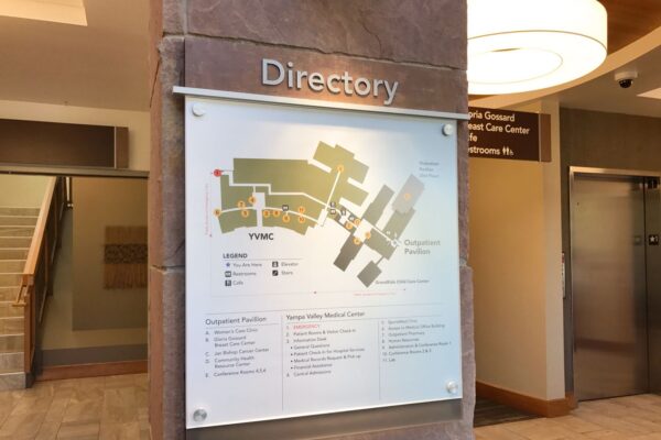 A building directory mounted on a wall, displaying a map and information about various locations within the building. The sign is labeled "Directory" and features floor plans and legend for easy navigation. The background includes stairs and an elevator.