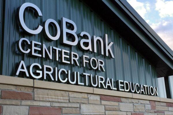 A building with a stone facade and green metal roof displays a sign that reads "CoBank Center for Agricultural Education."