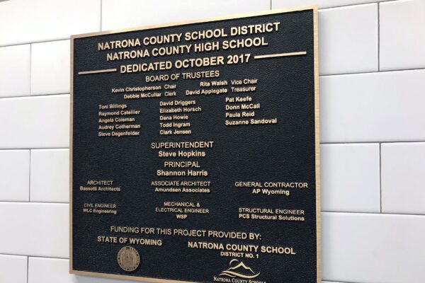 A bronze dedication plaque on a tiled wall reads, “Natrona County School District, Natrona County High School, Dedicated October 2017." It lists the Board of Trustees, Superintendent, Principal, Associate Principal, General Contractor, and Structural Engineer details.