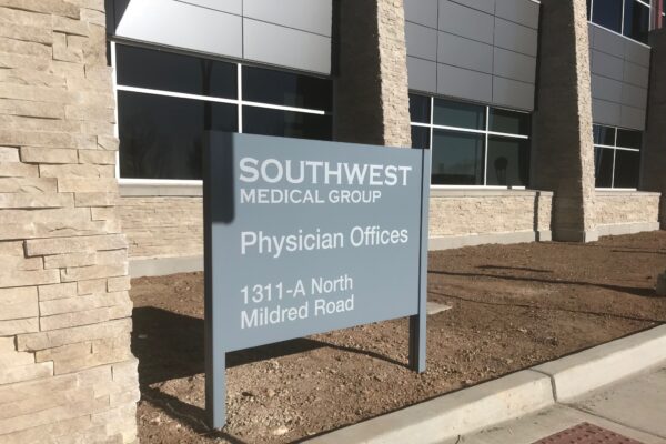 A sign outside a building reads "Southwest Medical Group Physician Offices, 1311-A North Mildred Road." The sign is positioned on a patch of bare ground in front of a modern building with stone and metal siding.
