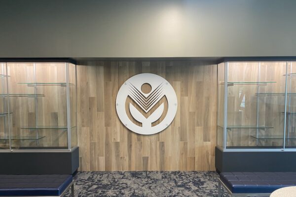 A wall with a wooden panel design displays a large, white, circular logo in the center. On either side of the logo are glass display cases with empty shelves. Blue cushioned benches with metal legs are positioned in front of the display cases.