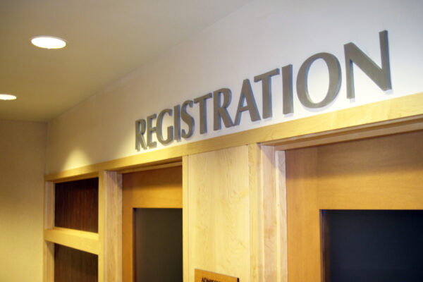 A hallway with a sign above two wooden doors that reads "REGISTRATION." The doors have frosted glass panels and are surrounded by light-colored wood. The lighting in the hallway appears to be warm, creating a welcoming atmosphere.