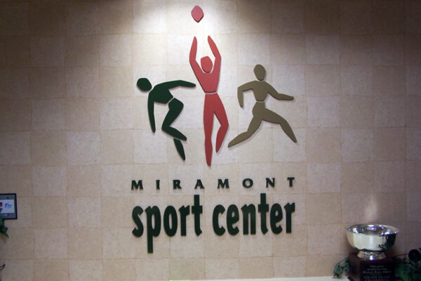 Wall sign for Miramont Sport Center featuring three stylized human figures in green, red, and brown engaged in sports activities. The words 'Miramont sport center' are prominently displayed beneath the figures.